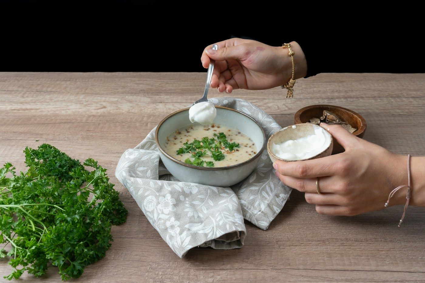 Mains qui ajoutent de la crème dans un bol de soupe, persil frais à côté