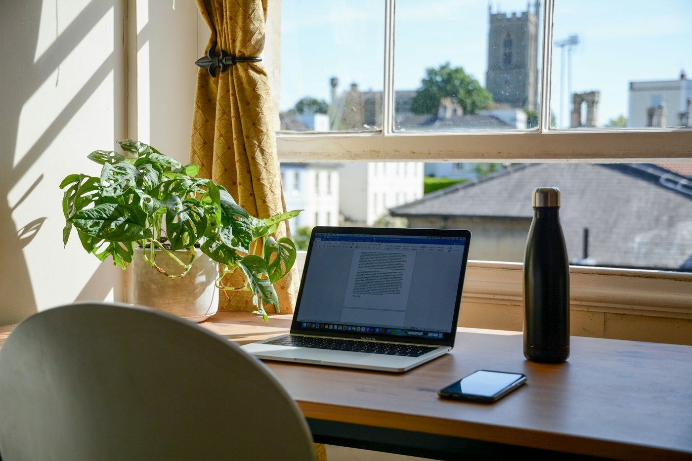 Ordinateur portable sur un bureau en bois devant une fenêtre, plante verte à côté